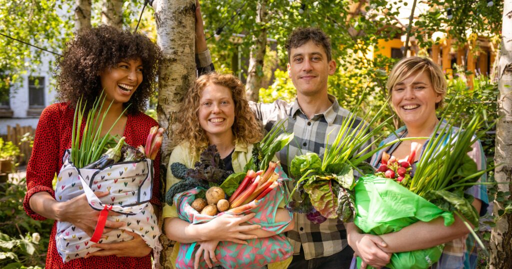 a group of smiling people from growing coop 'Growing Communities' in hackney are holding large amounts of organic, locally grown vegetables